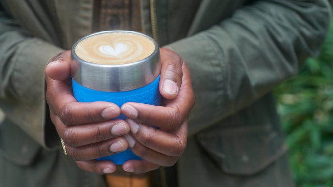 A person holding a reusable cup filled with coffe